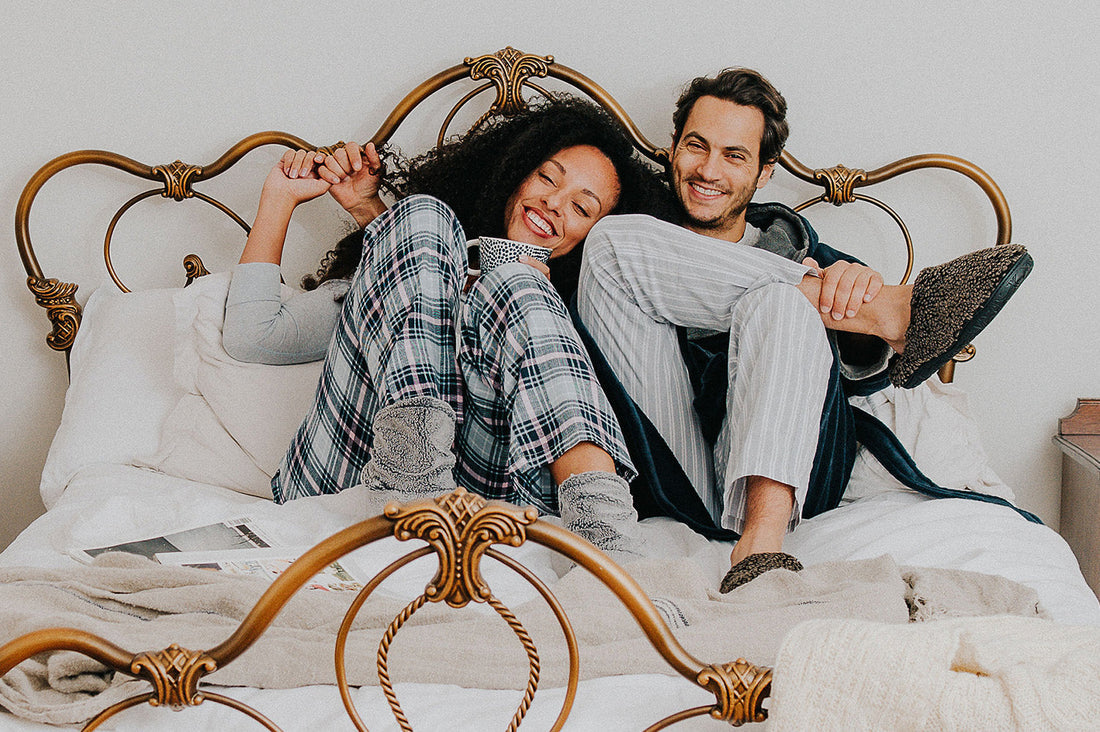 A couple curled up in bed at wearing a nightware and a dressing gown