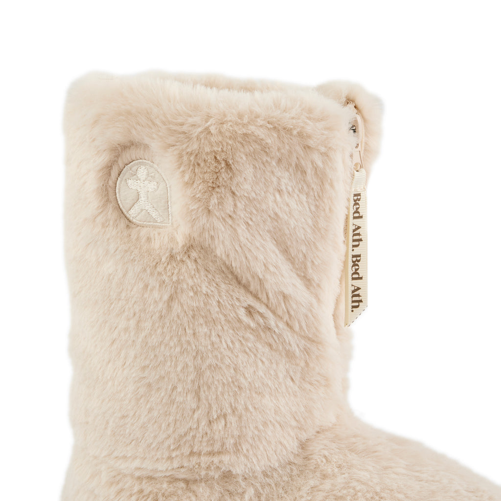 Close-up of a beige fuzzy boot with a brand logo on a white background