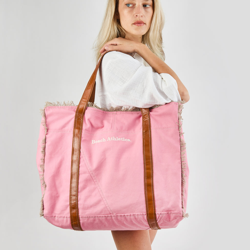 Bonnie: a pink washed canvas beach bag with frayed raw edges, tan leather handles and trim, and an embroidered Beach Athletics logo, shown from another angle