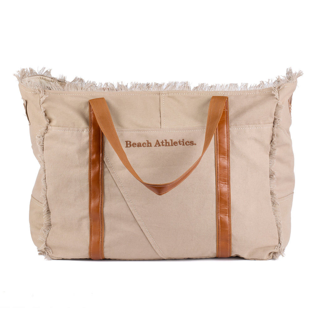 Bonnie: a beige washed canvas beach bag with frayed raw edges, tan leather handles and trim, and an embroidered Beach Athletics logo, front view