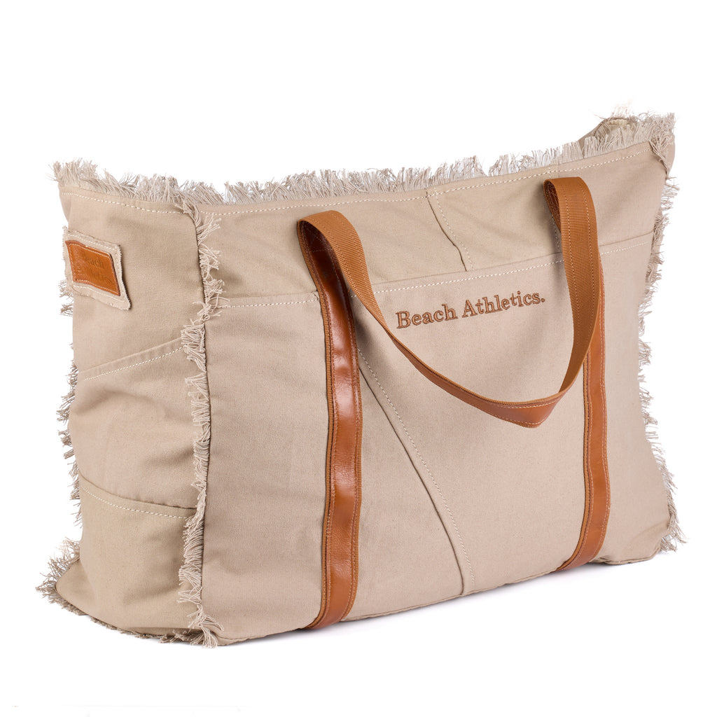 Bonnie: a beige washed canvas beach bag with frayed raw edges, tan leather handles and trim, and an embroidered Beach Athletics logo, shown at an angle