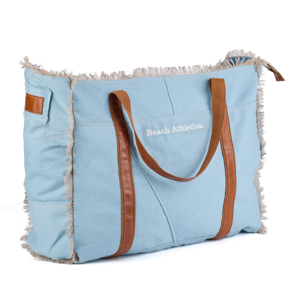 Bonnie: a blue washed canvas beach bag with frayed raw edges, tan leather handles and trim, and an embroidered Beach Athletics logo, shown in full from a second angle