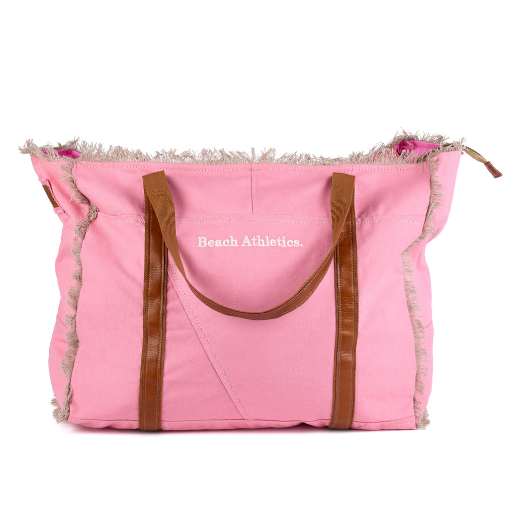 Bonnie: a pink washed canvas beach bag with frayed raw edges, tan leather handles and trim, and an embroidered Beach Athletics logo, front view, second angle