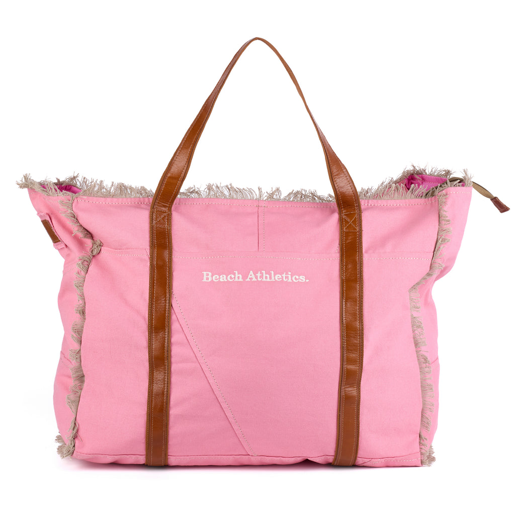 Bonnie: a pink washed canvas beach bag with frayed raw edges, tan leather handles and trim, and an embroidered Beach Athletics logo, front view with the handles raised