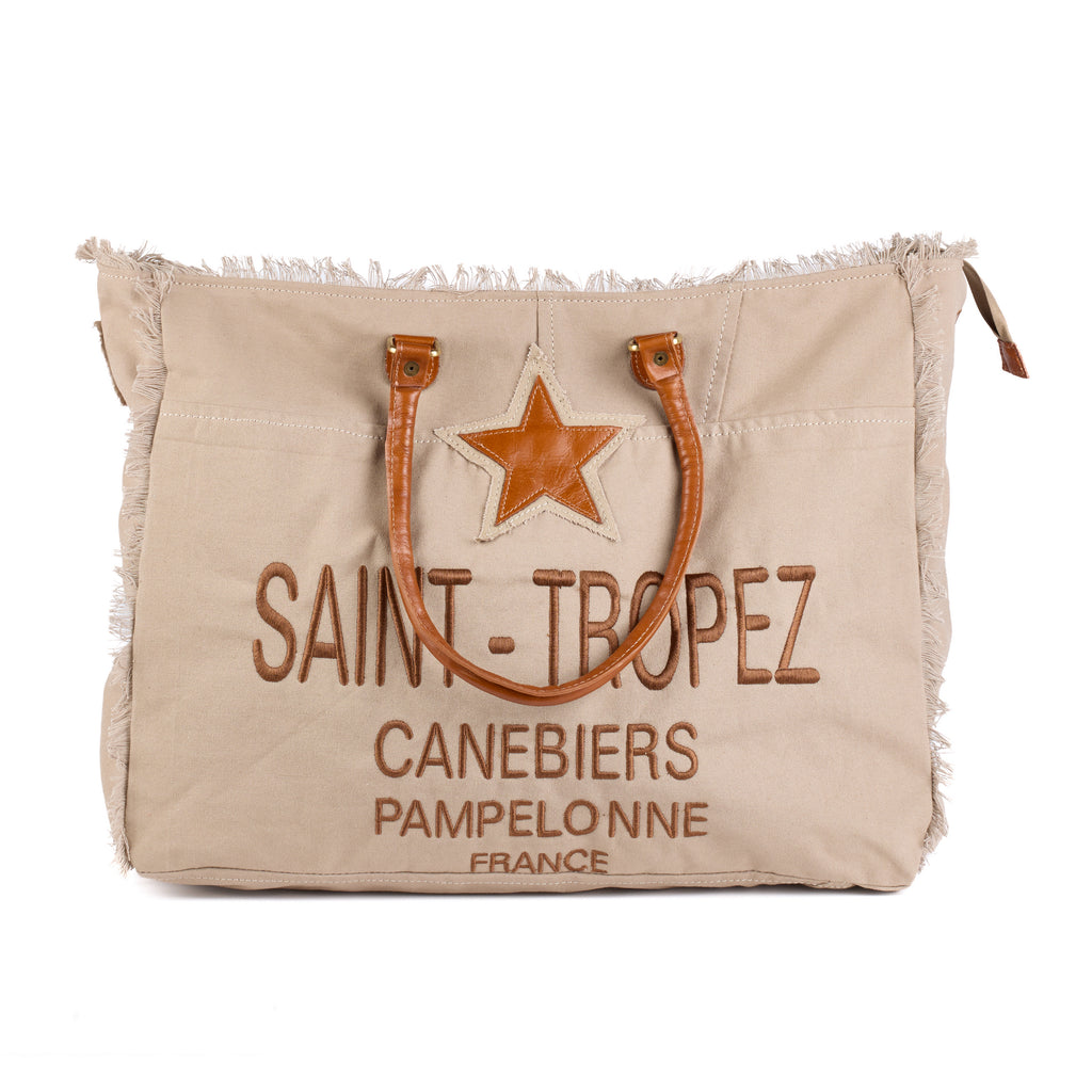 Casey: a beige washed canvas beach bag with frayed raw edges, a tan leather star patch and embroidered Saint-Tropez Canebiers Pampelonne France lettering, front view