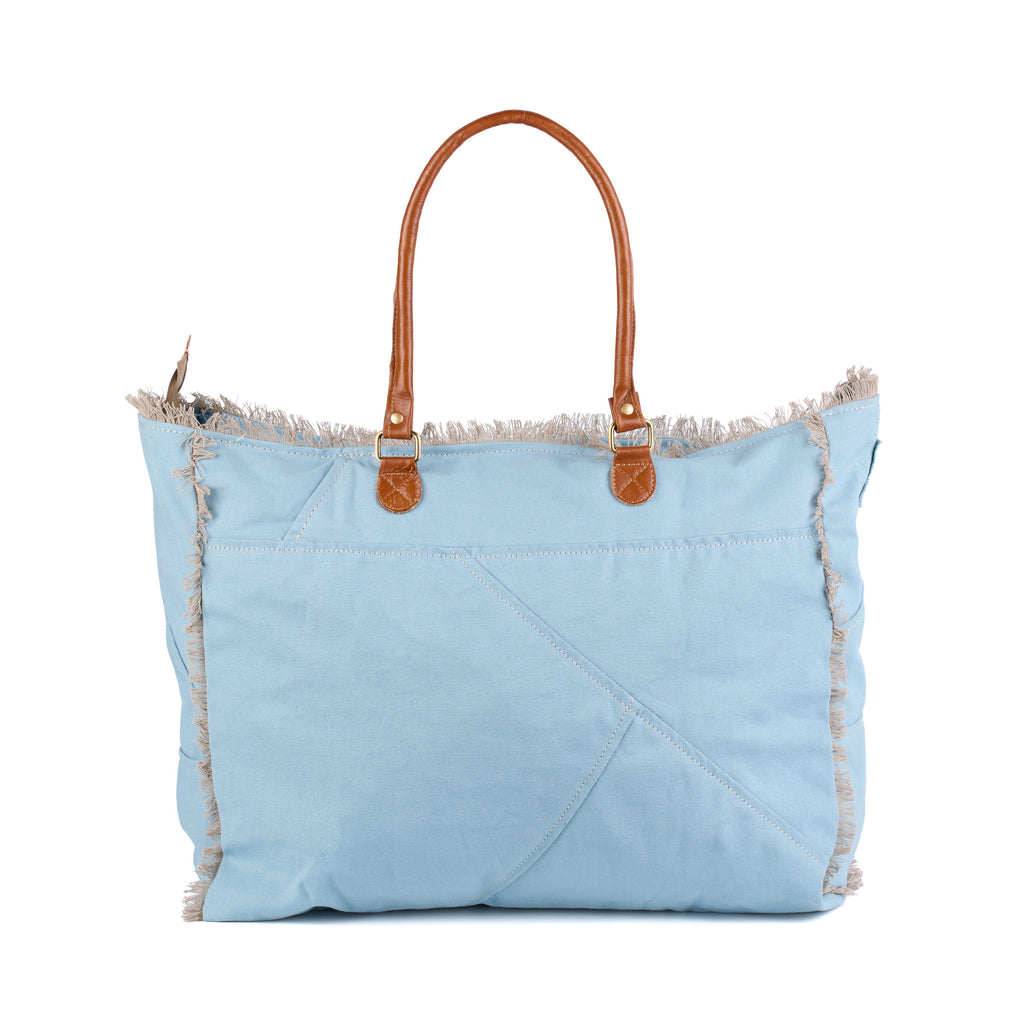 Casey: a blue washed canvas beach bag with frayed raw edges, a tan leather star patch and embroidered Saint-Tropez Canebiers Pampelonne France lettering, back view