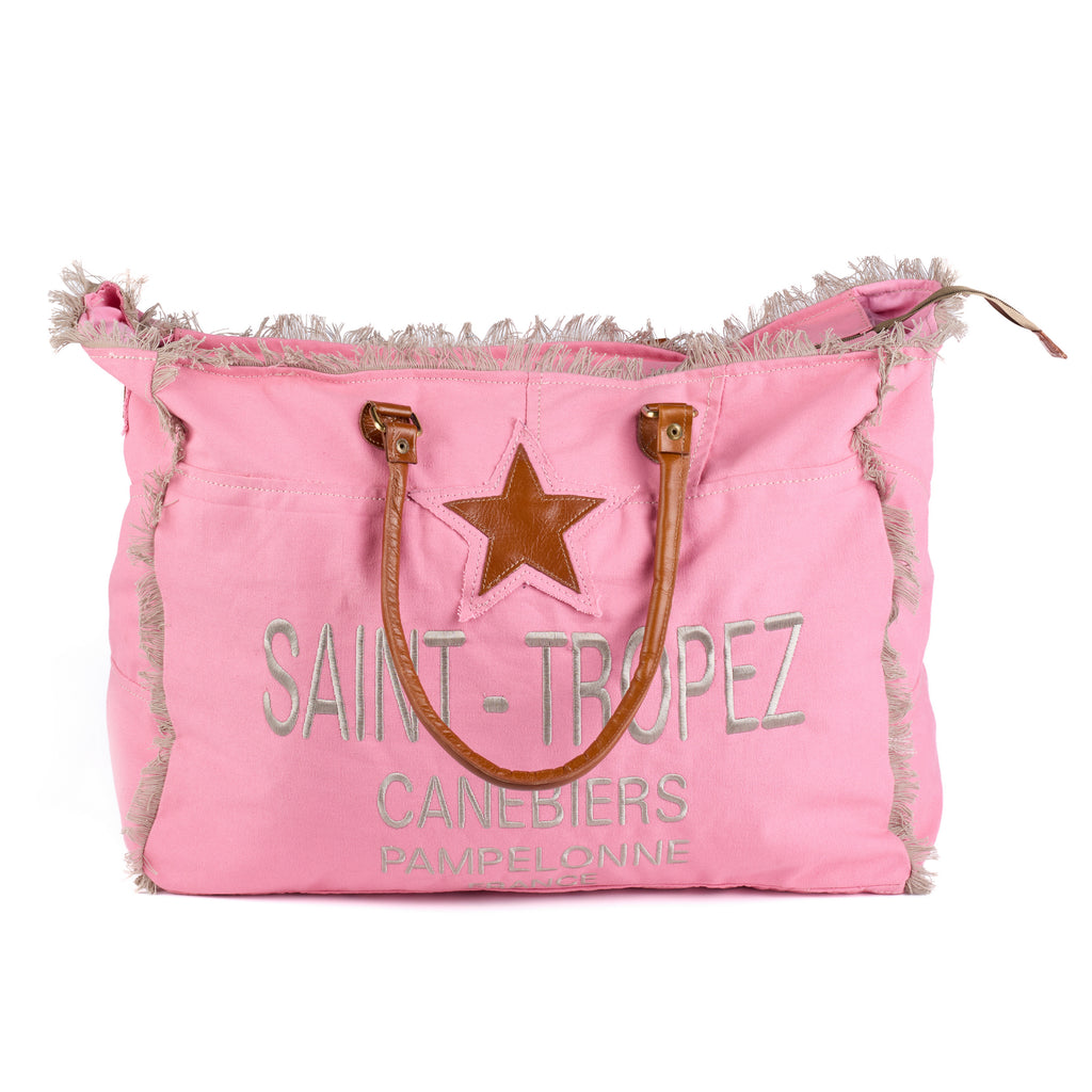 Casey: a pink washed canvas beach bag with frayed raw edges, a tan leather star patch and embroidered Saint-Tropez Canebiers Pampelonne France lettering, front view