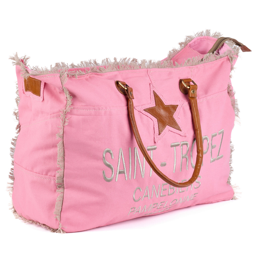 Casey: a pink washed canvas beach bag with frayed raw edges, a tan leather star patch and embroidered Saint-Tropez Canebiers Pampelonne France lettering, shown at an angle