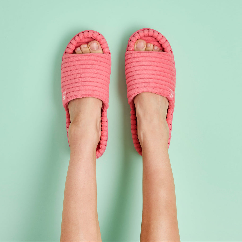 A top-down view of a person's feet wearing pink ribbed slide sandals on a solid mint green background.