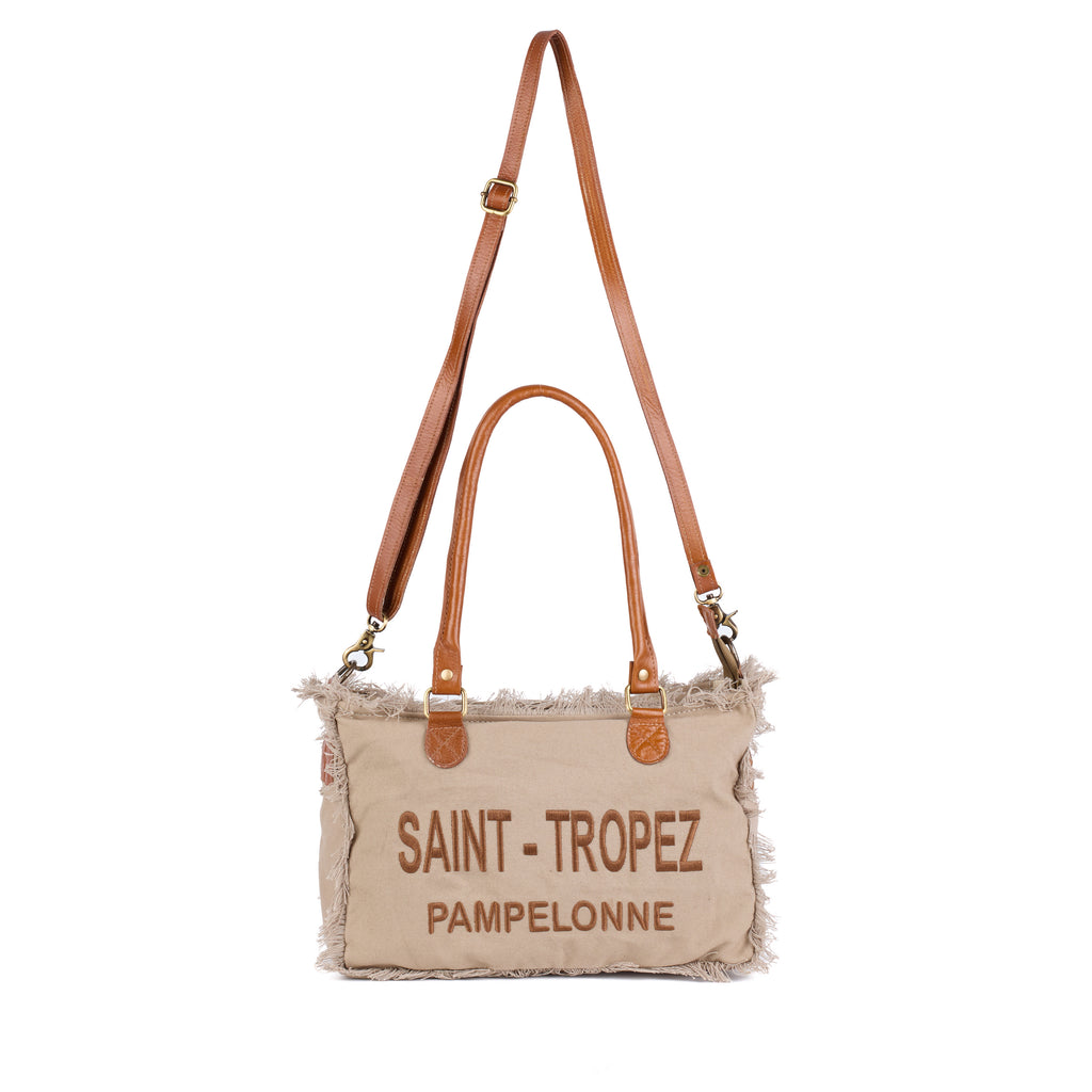 Lani: a beige washed canvas shoulder bag with frayed raw edges, tan leather trim and embroidered Saint-Tropez Pampelonne lettering, front view, shown in full