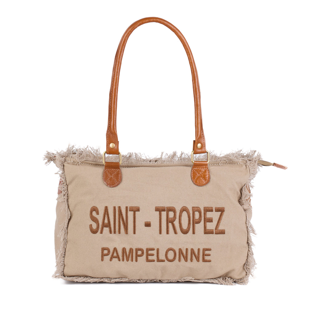 Lani: a beige washed canvas shoulder bag with frayed raw edges, tan leather trim and embroidered Saint-Tropez Pampelonne lettering, front view with the handles raised