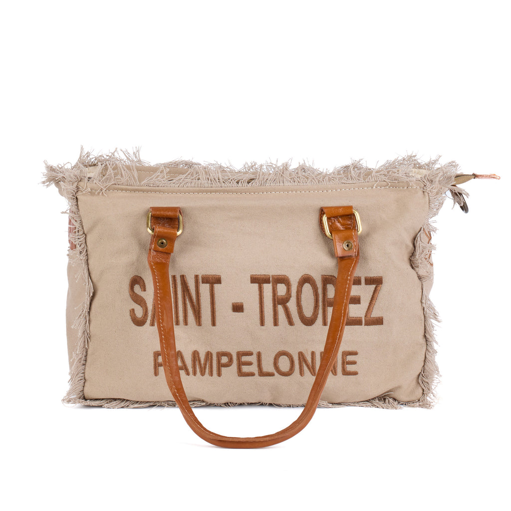Lani: a beige washed canvas shoulder bag with frayed raw edges, tan leather trim and embroidered Saint-Tropez Pampelonne lettering, front view