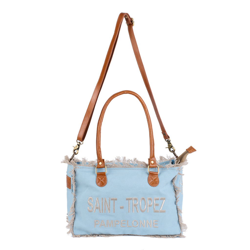 Lani: a blue washed canvas shoulder bag with frayed raw edges, tan leather trim and embroidered Saint-Tropez Pampelonne lettering, front view, shown in full