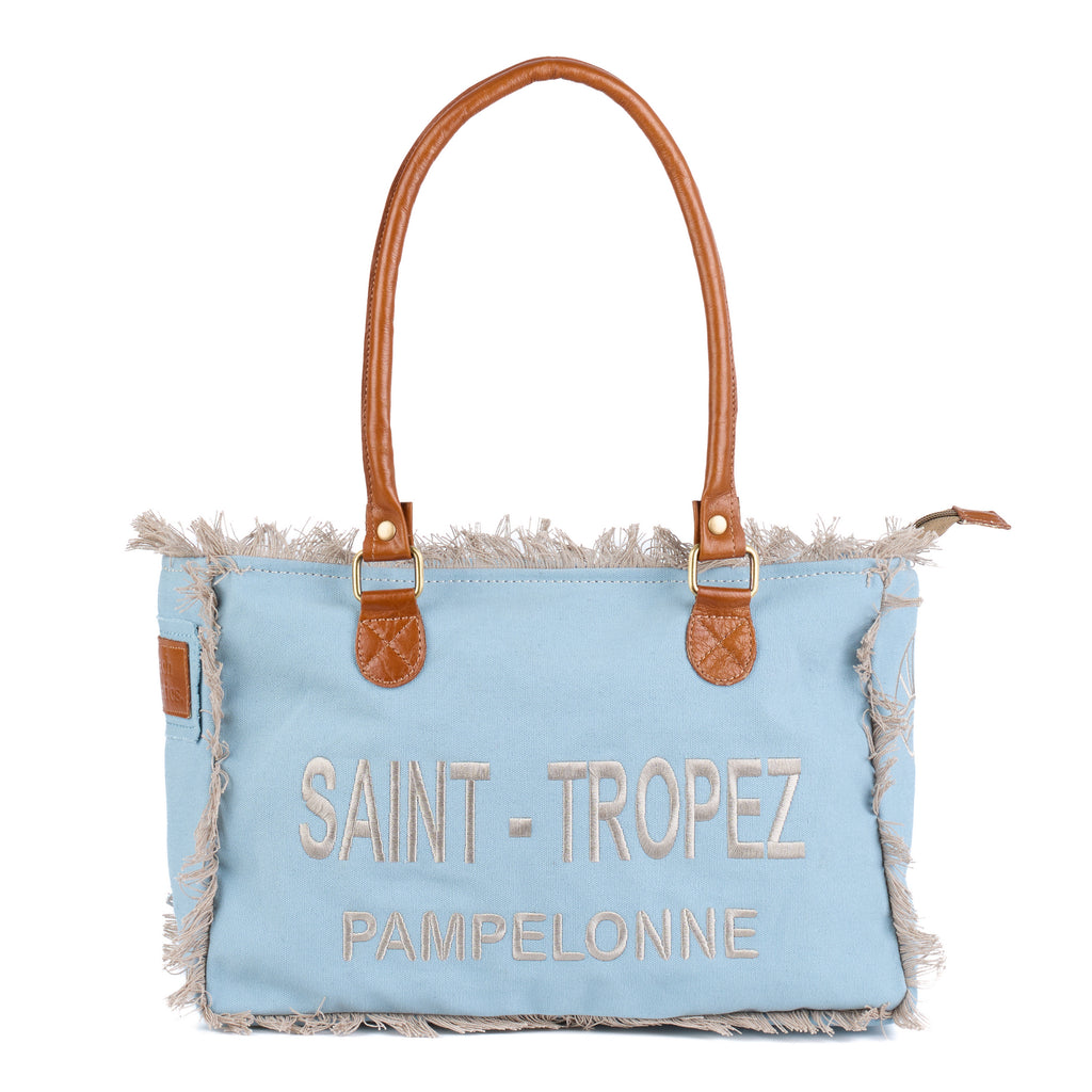 Lani: a blue washed canvas shoulder bag with frayed raw edges, tan leather trim and embroidered Saint-Tropez Pampelonne lettering, front view with the handles raised