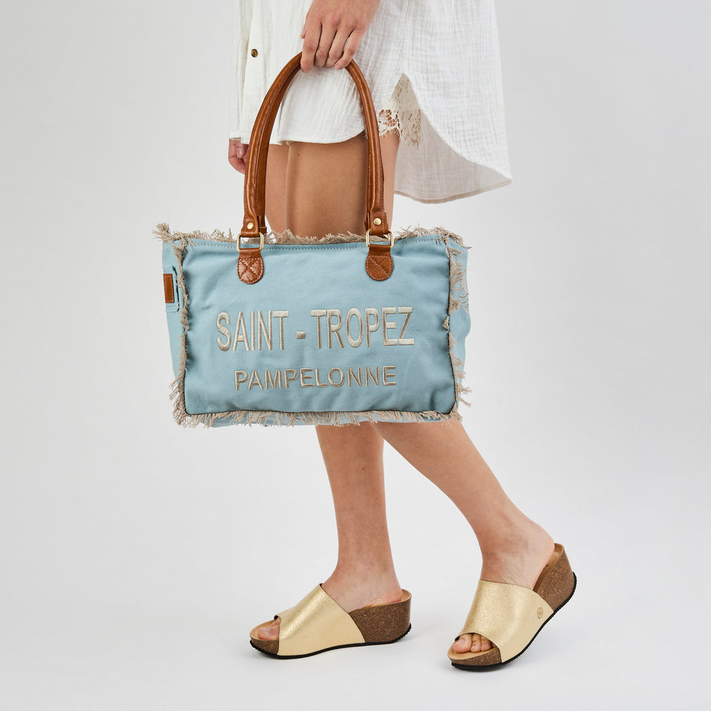 Lani: a blue washed canvas shoulder bag with frayed raw edges, tan leather trim and embroidered Saint-Tropez Pampelonne lettering, shown from another angle