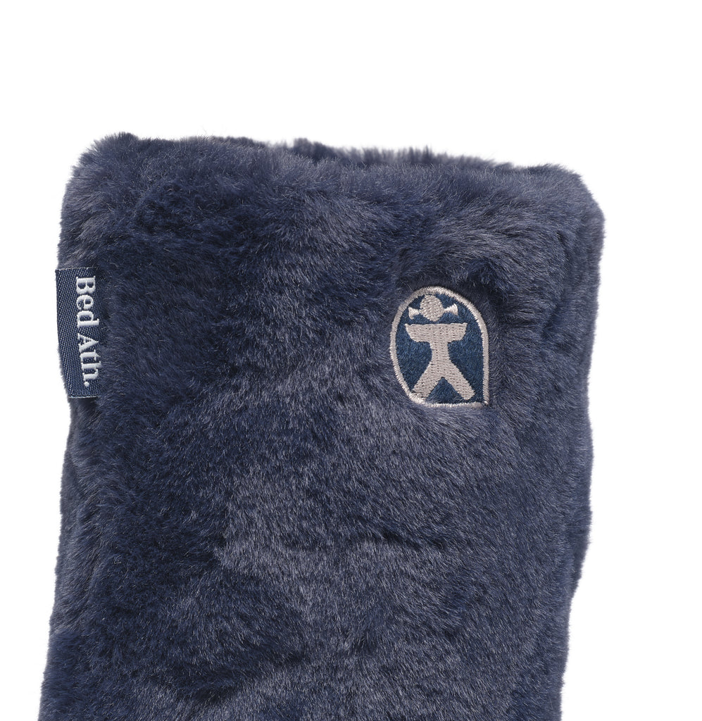 A close-up of a dark navy blue faux fur sleeve or cover, featuring a silver embroidered Bed Bath brand logo on the front and a black fabric side tag with white text.