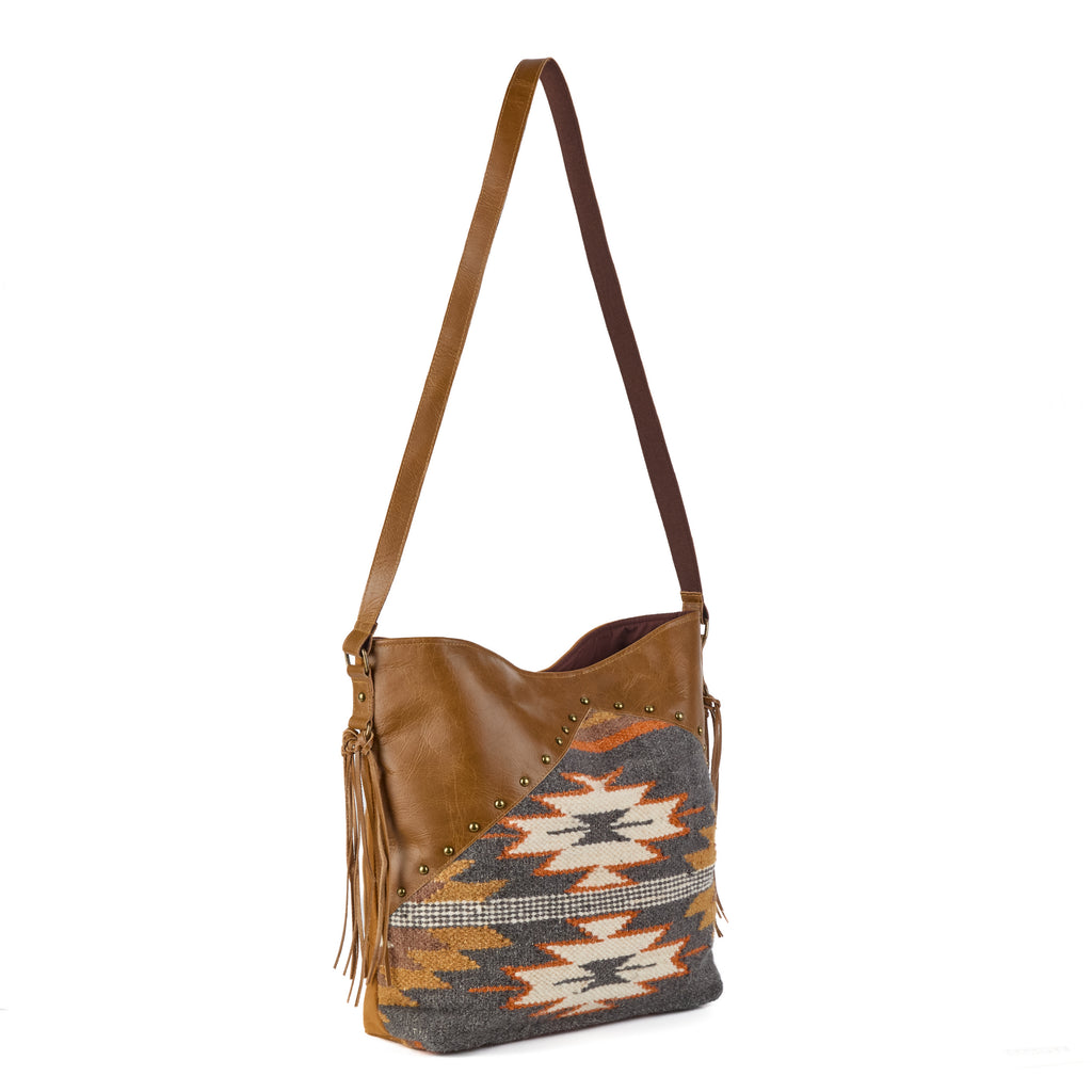 Monterey: a boho shoulder bag mixing tan leather (with brass stud detailing) and a grey, orange and cream aztec-pattern wool weave, with a suede fringe tassel, shown from another angle