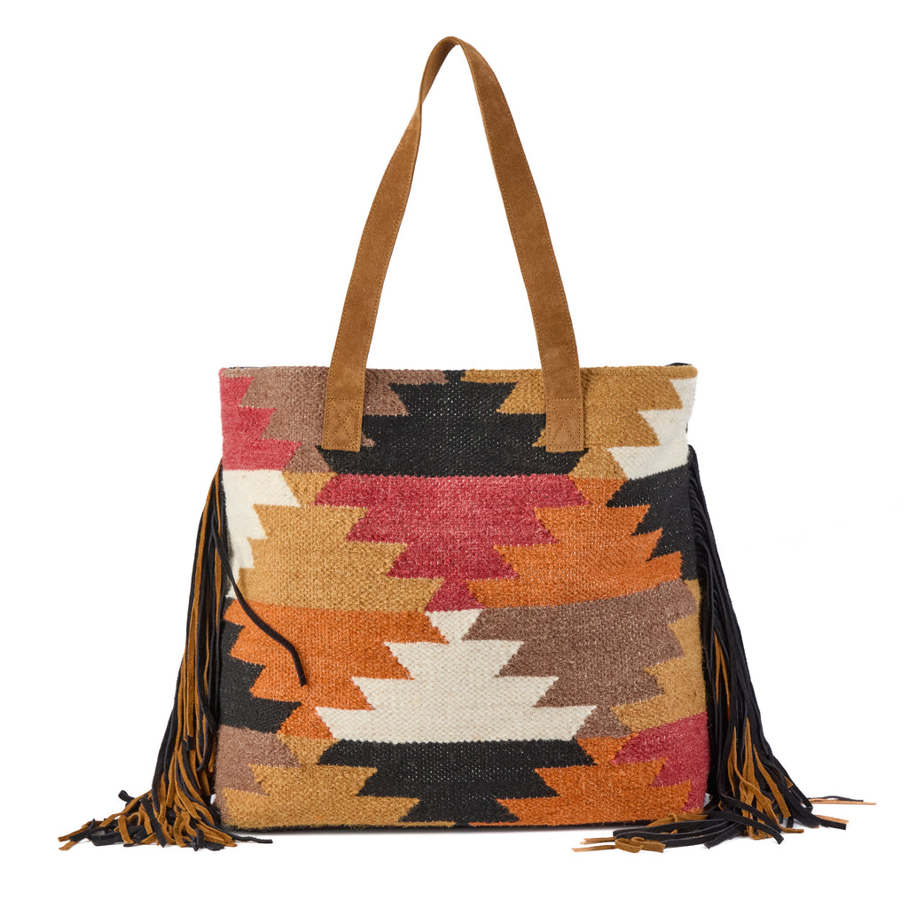 Montreux: a boho tote bag in a black, red, tan and cream aztec-pattern weave, with fringe trim along the base and suede tote handles, shown from another angle
