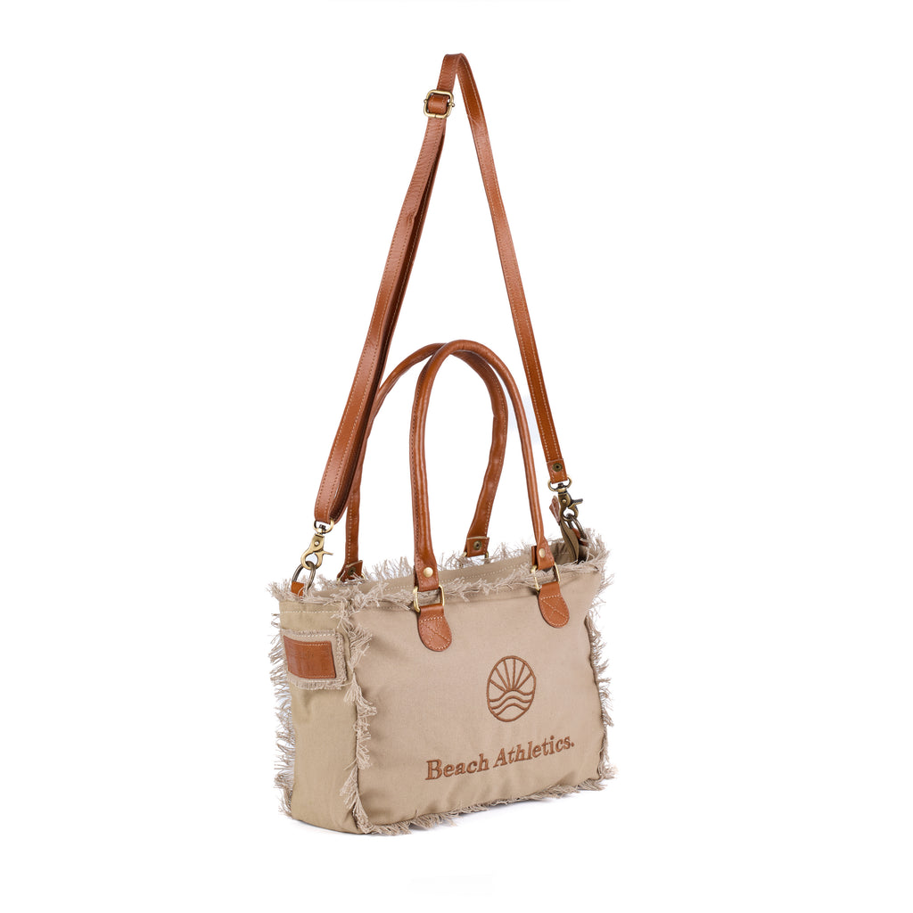 Shauni: a beige washed canvas shoulder bag with frayed raw edges, tan leather trim and an embroidered sunrise Beach Athletics logo, shown in full from an angle