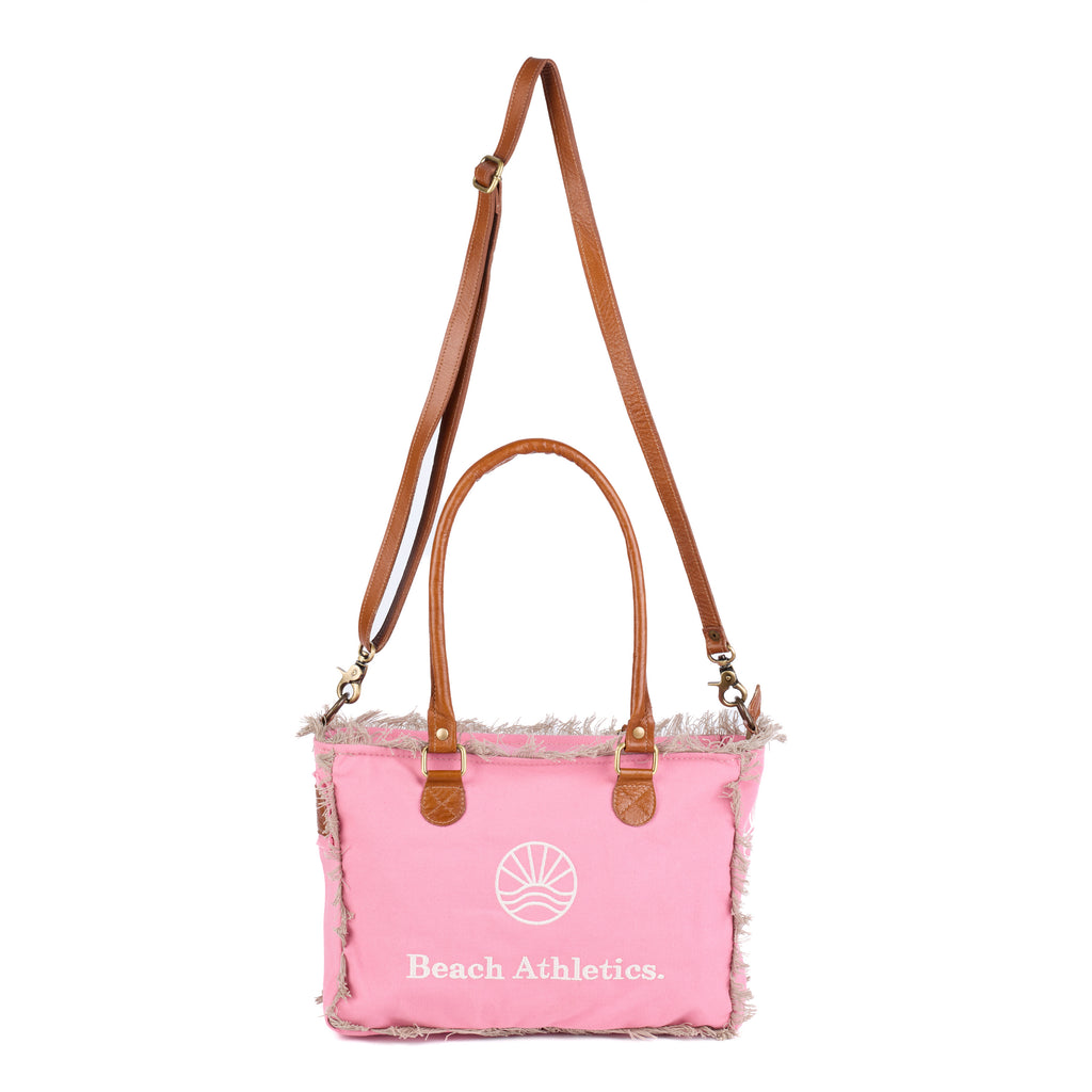 Shauni: a pink washed canvas shoulder bag with frayed raw edges, tan leather trim and an embroidered sunrise Beach Athletics logo, front view, shown in full